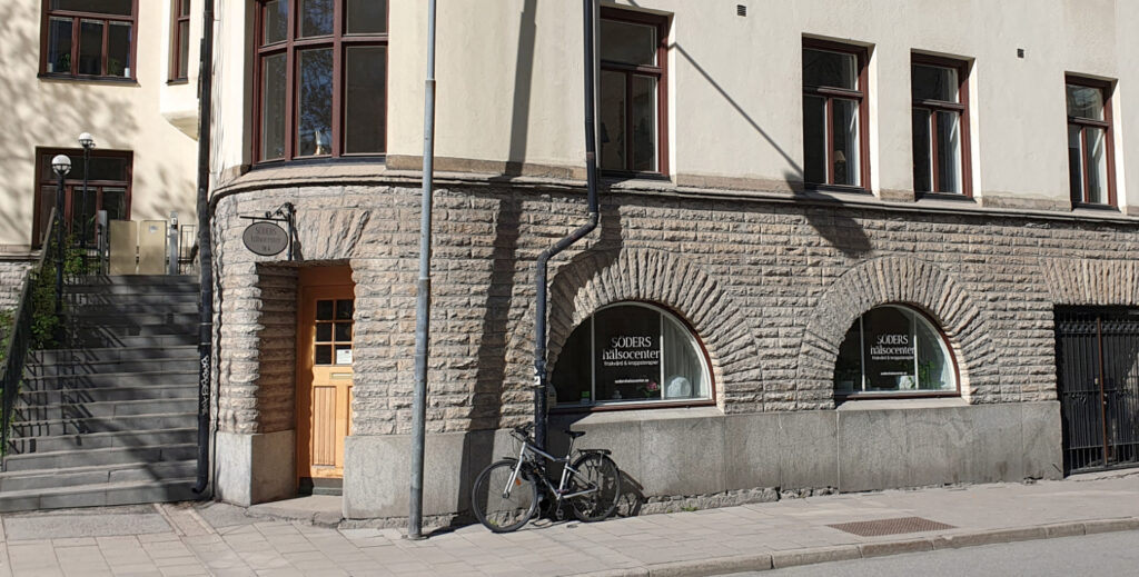 Söders Hälsocenter sett från gatan, en trädörr och två halvrunda skyltfönster